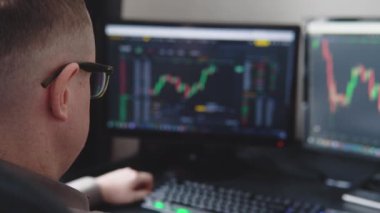 Bearded man trader wearing eyeglasses sitting at desk at office monitoring stock market looking at monitors analyzing candle bar price