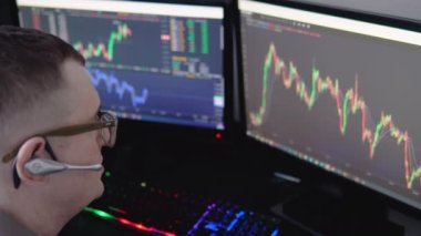 Borsa borsası. Modern ofisinde çalışırken bilgisayar ekranındaki verileri kalemle işaret eden ve bir elinde Bitcoin tutan gözlüklü genç profesyonel tüccarın geri görünümü.