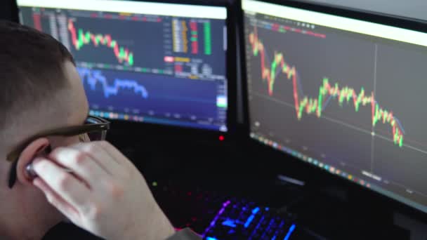 証券取引所 ペンでコンピュータ画面上のデータを指し 彼の近代的なオフィスで働いている間 片手にビットコインを保持する眼鏡で若いプロのトレーダーのバックビュー — ストック動画
