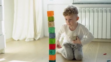 Little boy building tower of block toys sitting on floor in sunny bedroom.