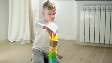 Little boy building tower of block toys sitting on floor in sunny bedroom. Child playing with colorful toy blocks. Kids play. Educational game for baby and toddler. Children build toy house.