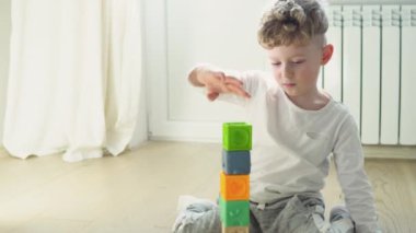 Little boy building tower of block toys sitting on floor in sunny bedroom