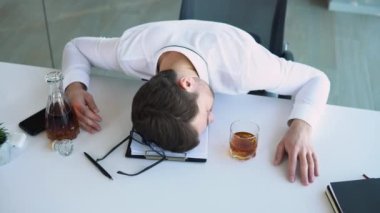 Alkolizm, içki konsepti. İş yerinde uyuyan sarhoş bir çalışan, bardağı alkolle tutan, seçici odaklı.