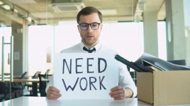 Dismissed worker holding cardboard sign poster Need work. Sad depressive distressed young guy suffers from anxiety, sadness because of losing job or business.