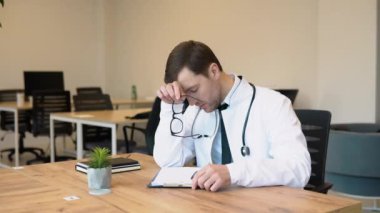 Stresli, olgun, beyaz üniformalı, steteskoplu, elleri kapalı, hastanede çalışma masasında oturan üzgün yaşlı bir doktor tıbbi yetersizlikten dolayı kendini suçlu ve çaresiz hissediyor..