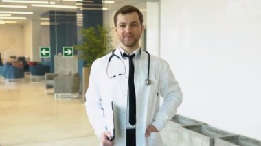 Beyaz tıp üniformalı, gülümseyen beyaz erkek doktor hastanede iyi hizmet veriyor. Klinikteki mutlu pratisyen hekimin ya da çocuk doktorunun portresi. Sağlık hizmetleri kavramı.