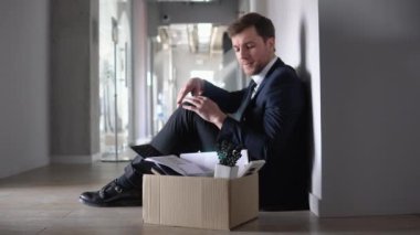 Fired business man or employee sitting frustrated and upset in the hallway near office with dismissal box