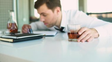 Alkolizm, içki konsepti. İş yerinde uyuyan sarhoş bir çalışan, bardağı alkolle tutan, seçici odaklı..