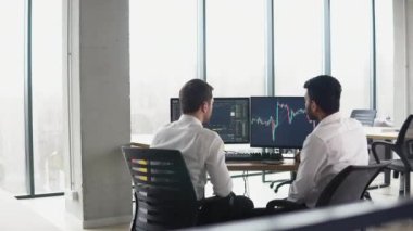 Çevrimiçi kripto para birimi indekslerini analiz eden iki çok ırklı yatırımcı. Çeşitli yöneticiler tüccarlar analistler ekranda bilgisayar grafikleriyle finansal büyüme pazarını tartışıyor.