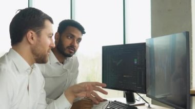 Çevrimiçi kripto para birimi indekslerini analiz eden iki çok ırklı yatırımcı. Çeşitli yöneticiler tüccarlar analistler ekranda bilgisayar grafikleriyle finansal büyüme pazarını tartışıyor.