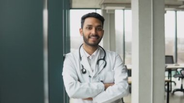 Portrait of smiling male indian student doctor with crossed arms wearing white coat.