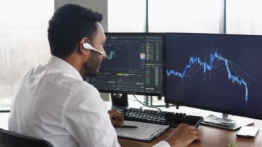 Side view of smart Indian crypto trader, investor, analyst broker, using pc analyzing digital cryptocurrency exchange, stock market charts, thinking of investing and funds risks