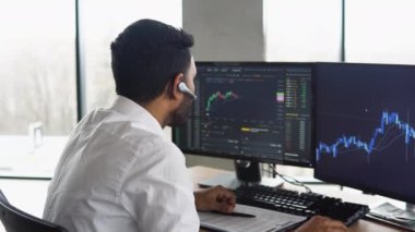 Side view of smart Indian crypto trader, investor, analyst broker, using pc analyzing digital cryptocurrency exchange, stock market charts, thinking of investing and funds risks