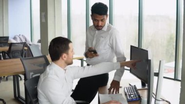 Manager consulting indian client with online technology at office meeting. Two diverse business men analysts partners talking, working together, discussing data management using computer