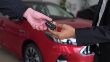 Indian car manager giving keys to customer at salon. Two men shaking hands for making deal. Close up of hands, blur background. Concept of car selling