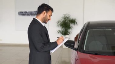 Indian salesman making deal signs a sales document in dealership office.