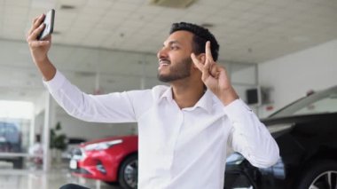 Indian man happily shoots a video near the car in a car dealership.