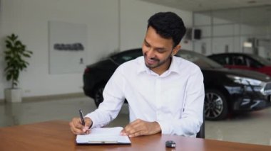 Hintli satıcı satış bürosunda otururken bir arabanın satış belgesini imzalıyor..