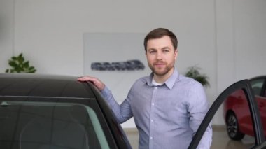 Satın almak için aracı seçen yakışıklı bir genç. Yeni lüks bir arabanın yanındaki galeride duran mutlu adam. Otomatik iş kavramı.