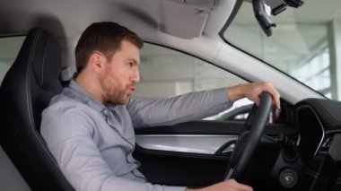 Komik bir alıcı araba galerisinde araba kullanıyormuş gibi yapar. Mutluluk ve pahalı satın alma kavramı.