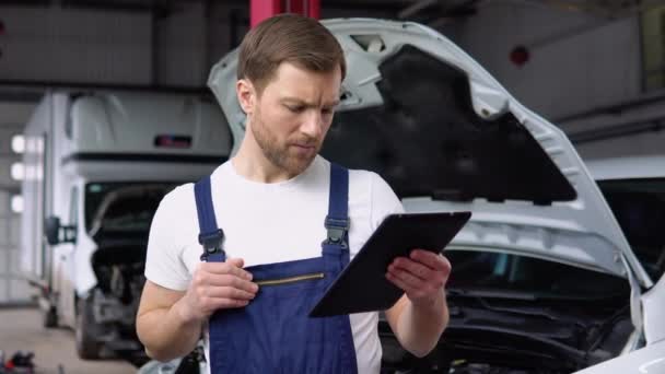 专业的汽车修理工 从事平板电脑的汽车维修服务 在汽车沙龙工作的穿制服的成年人 — 图库视频影像
