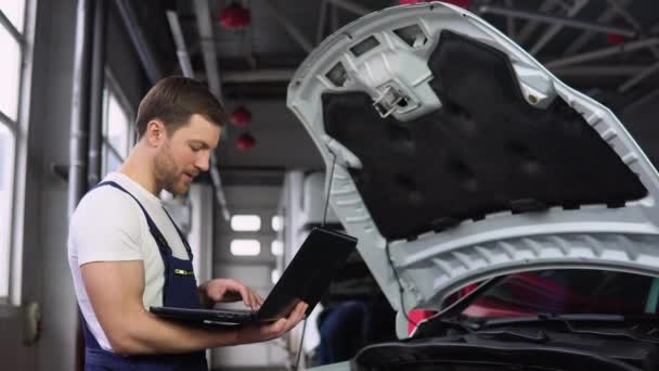 专业汽车修理工用笔记本电脑从事汽车维修服务 在汽车沙龙工作的穿制服的成年人 — 图库视频影像