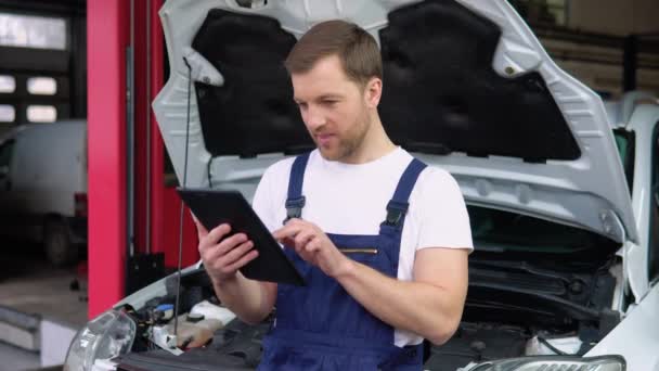 专业的汽车修理工 从事平板电脑的汽车维修服务 在汽车沙龙工作的穿制服的成年人 — 图库视频影像