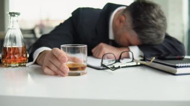 Alkolizm, içki konsepti. İş yerinde uyuyan sarhoş bir çalışan, elinde alkolle bardak tutuyor.