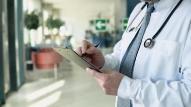 Beyaz önlüklü ve gözlüklü orta yaşlı baş doktor kağıt günlüğe notlar yazıyor, kapat..