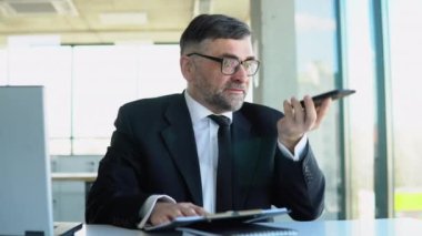 Angry boss shouts to the employee while looking at phone, dismisses the subordinate, a businessman in a business suit sits at a table in a modern office