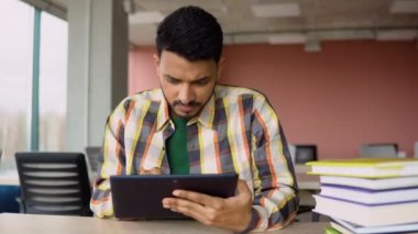 Hintli öğrenci bir okul kütüphanesinde okuyor. Bir tablet kullanıyor ve internetten okuyor..
