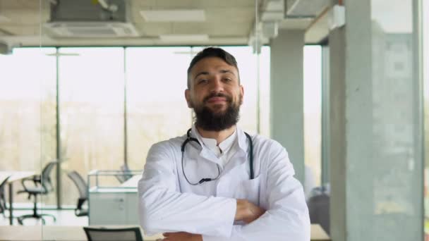 在诊所里 一个快乐的阿拉伯医生对着相机微笑 双手交叉听诊器的画像 有信心的心脏病医生站在医院里 成功的医疗生涯 — 图库视频影像
