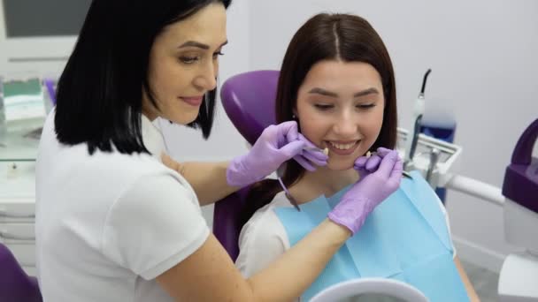 歯医者は特別なスケールから歯の色を選択します 女の子の患者と入れ歯の歯の日陰の選択 — ストック動画