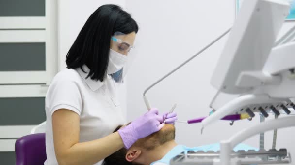 Kvinnlig Tandläkare Ansiktsmask Och Glasögon Som Gör Behandling För Manliga — Stockvideo
