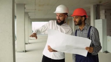 Arap mimar Hintli inşaatçıya inşaat planını anlatıyor. Ustabaşı binayı ciddiyetle işaret ediyor.