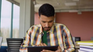 Hintli öğrenci bir okul kütüphanesinde okuyor. Bir tablet kullanıyor ve internetten okuyor.