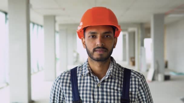建設現場に立って カメラを見て安全ヘルメットを身に着けている制服を着たインド人アジア人労働者を確信 — ストック動画