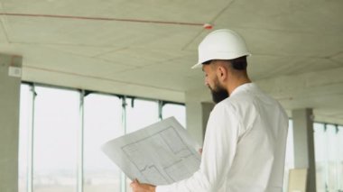 Ciddi çekici Arap endüstriyel mühendisi. Kasketli. Bir gökdelen inşaatında proje çizimleri var. Profesyonel ve endüstri, mimarlık işi, fabrikada çalışan işçiler.