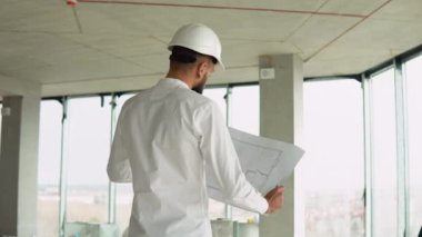 Ciddi çekici Arap endüstriyel mühendisi. Kasketli. Bir gökdelen inşaatında proje çizimleri var. Profesyonel ve endüstri, mimarlık işi