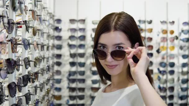 Νεαρή Γυναίκα Δοκιμάζει Νέα Γυαλιά Ηλίου Οπτικό Κατάστημα Φόντο Βιτρίνα — Αρχείο Βίντεο
