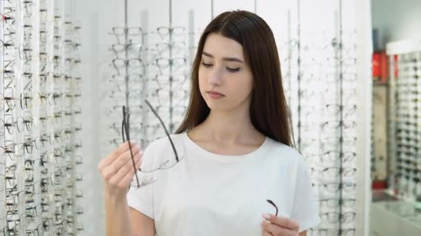 Vzrušená Dívka Nemůže Vybrat Brýle Obchodě Dívka Bílém Tričku Kupuje — Stock video