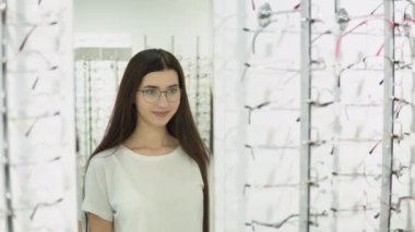 Yeni gözlüklü güzel bir kadın modern optik mağazada aynaya bakıyor..