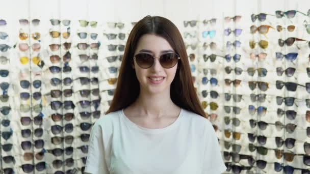不同眼镜样式的橱窗背景下的新太阳镜中年轻女子的画像 — 图库视频影像