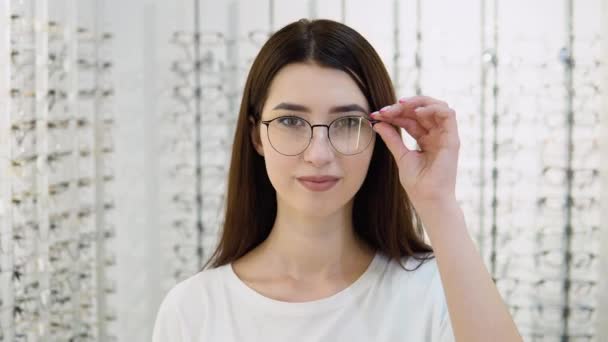 Νεαρή Γυναίκα Διαλέγει Γυαλιά Στο Μαγαζί Ένα Κορίτσι Λευκό Μπλουζάκι — Αρχείο Βίντεο