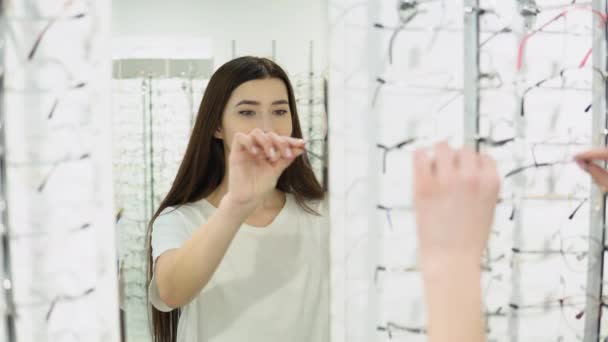 在现代光学商店里 一位漂亮的年轻女子正在挑选镜框 目光炯炯 — 图库视频影像