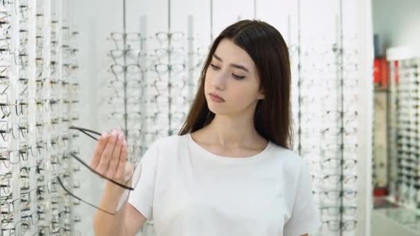 Vzrušená Dívka Nemůže Vybrat Brýle Obchodě Dívka Bílém Tričku Kupuje — Stock video