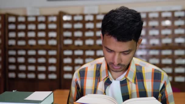 図書館で真剣な面持ちで本を読んでいる若いインド人の学生 真剣に考えられた学生は試験の準備をする — ストック動画