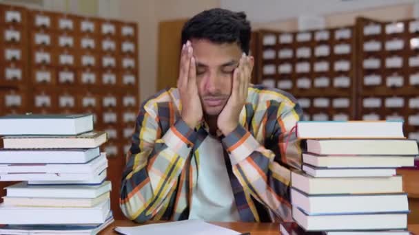 疲惫的印第安学生穿着休闲装 坐在图书馆的书桌前看书 双手抱头 看起来厌倦了看书 认真思考准备考试的学生 — 图库视频影像