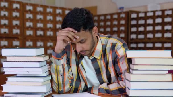 身穿休闲装的疲惫不堪的印第安学生坐在图书馆的书桌前看书 双手抱头 看起来厌倦了看书 — 图库视频影像