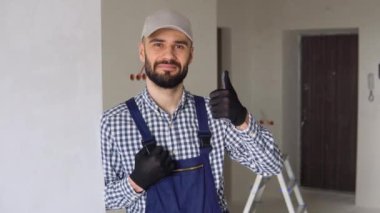 Üniformalı genç tamirci dairenin içinde dikilip kameraya bakıyor..